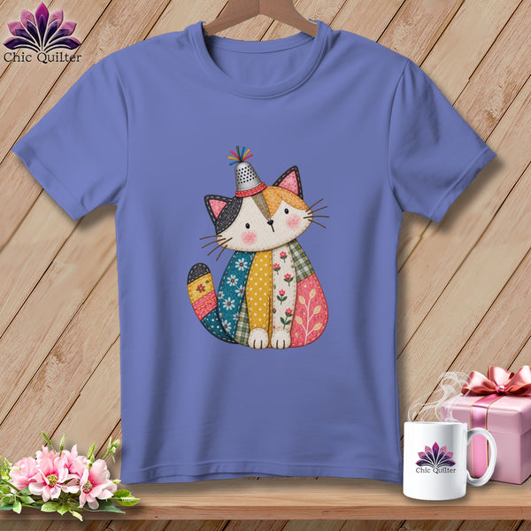 A periwinkle t-shirt features a graphic of a stitched patchwork cat wearing a thimble hat.