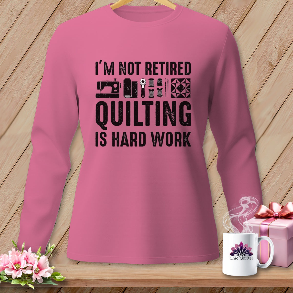 Pink long-sleeve shirt with black text and quilting graphics: "I'M NOT RETIRED QUILTING IS HARD WORK."