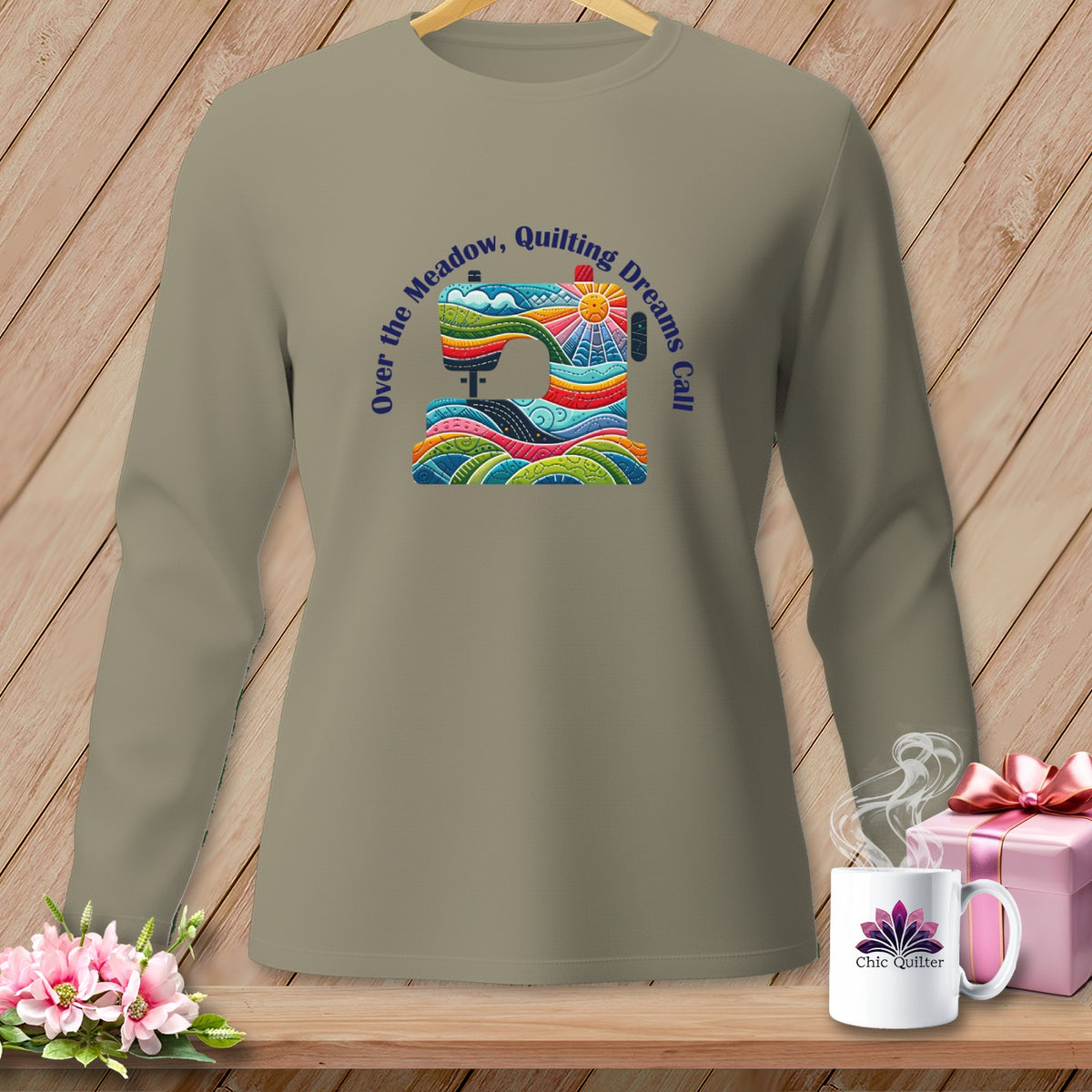 Taupe long-sleeve shirt with colorful sewing machine and "Over the Meadow, Quilting Dreams Call" text.