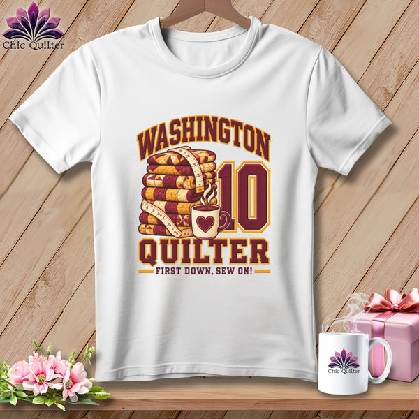 A white t-shirt features a graphic with stacked quilts, a measuring tape, coffee cup, and text reading Washington Quilter, First Down, Sew On!