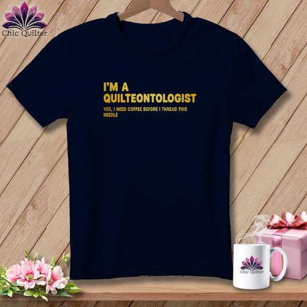 Navy t-shirt with yellow text: "I'M A QUILTEONTOLOGIST YES, I NEED COFFEE BEFORE I THREAD THIS NEEDLE."