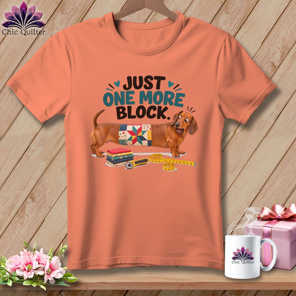 Dachshund wearing a quilt block with text "JUST ONE MORE BLOCK."