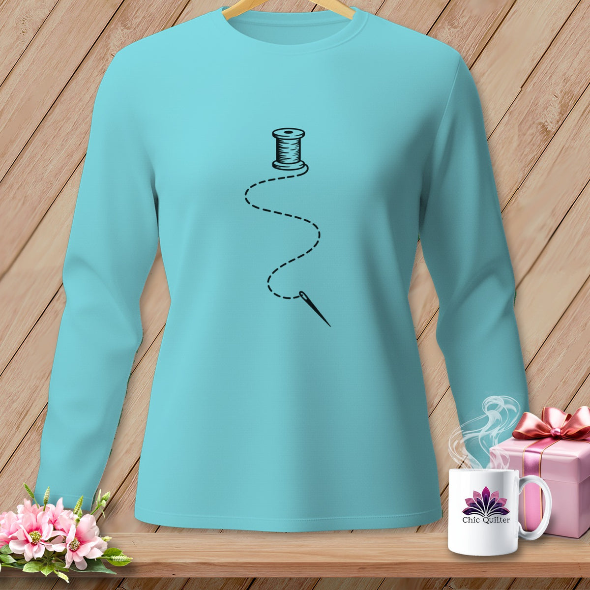 Teal long-sleeve shirt with black spool of thread, needle, and dashed line design.