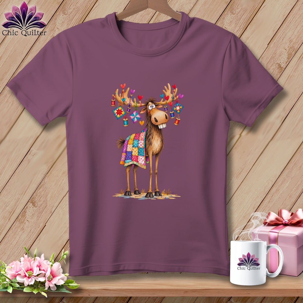 A plum-colored crewneck t-shirt featuring a whimsical cartoon moose with a quilt draped over it.