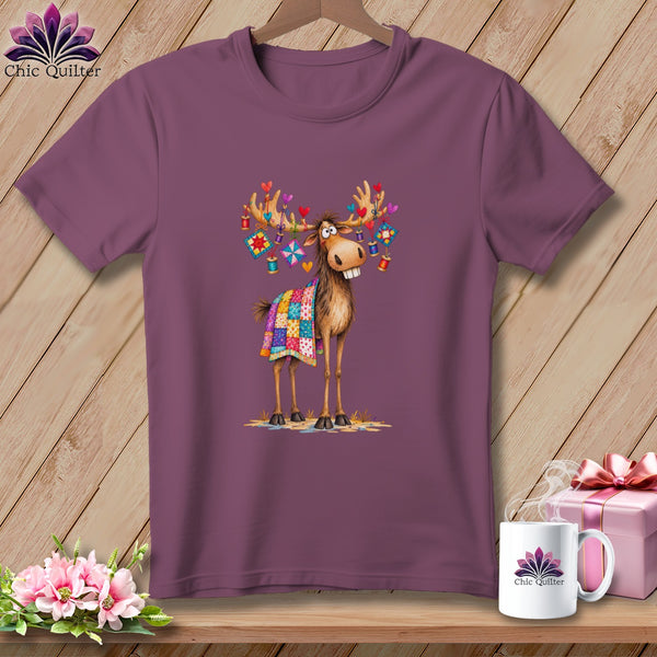 A plum-colored crewneck t-shirt featuring a whimsical cartoon moose with a quilt draped over it.
