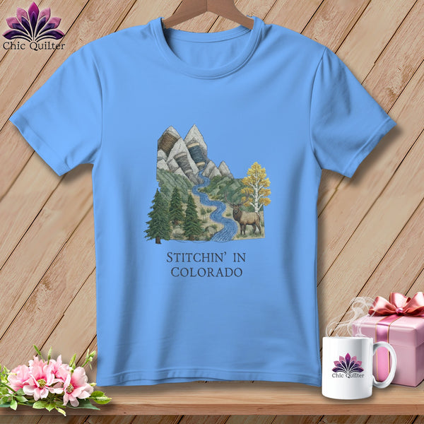 Light blue t-shirt with mountain landscape, elk, and text "Stitchin' in Colorado".