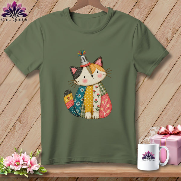 An olive green t-shirt features a colorful, quilted cat illustration wearing a thimble hat.