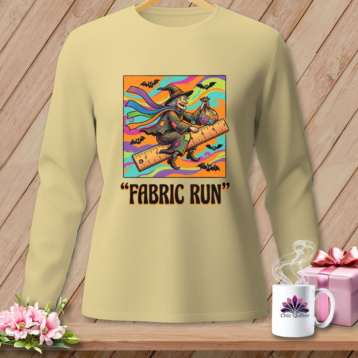 Witch on a ruler with bats and "FABRIC RUN" text on tan shirt.