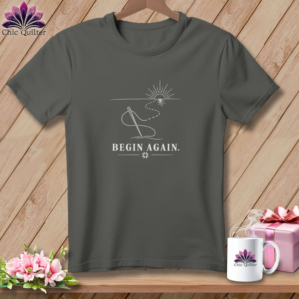 Dark grey t-shirt with needle, thread, sunrise, and "BEGIN AGAIN." text.