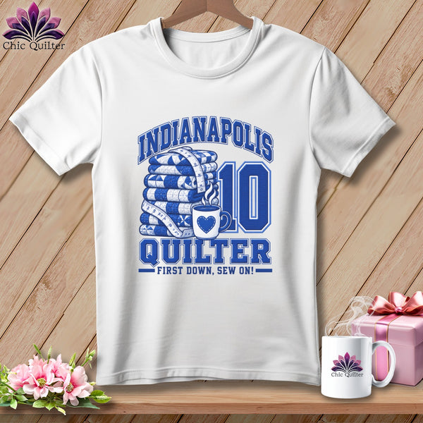 A white t-shirt features blue text reading Indianapolis Quilter, First Down, Sew On, alongside stacked quilts, a coffee mug, and the number ten.