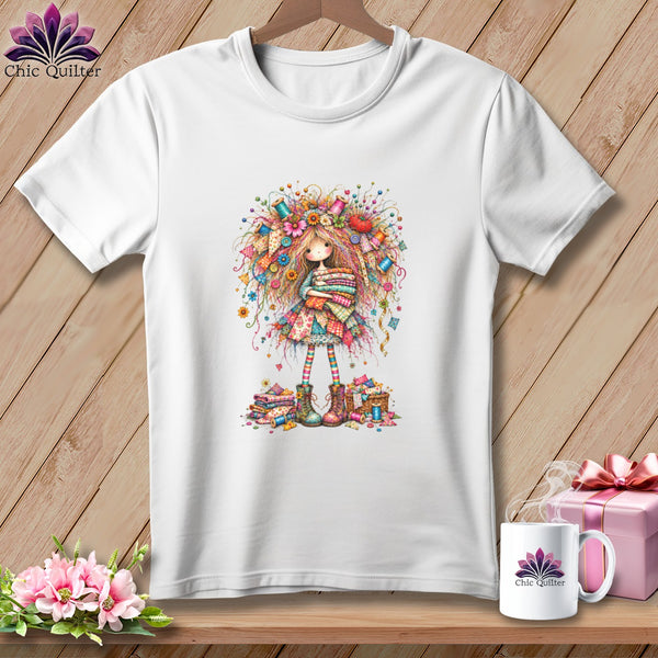 A white t-shirt features a colorful illustration of a whimsical doll surrounded by sewing supplies.