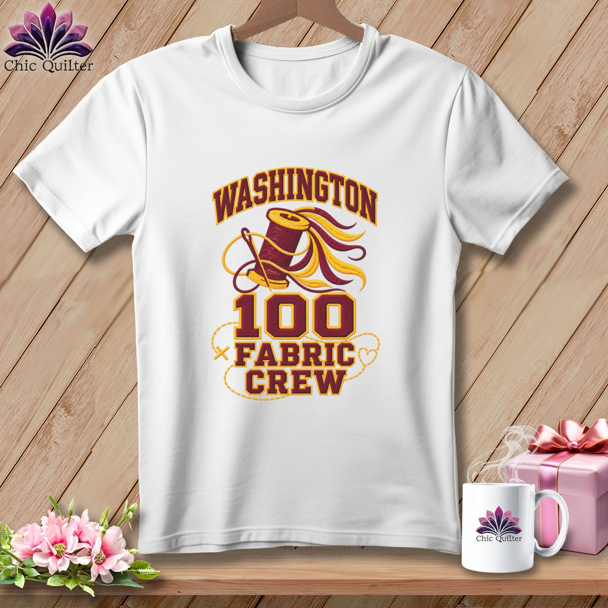 A white t-shirt on a wooden background features a design reading Washington 100 Fabric Crew with a thread spool graphic.