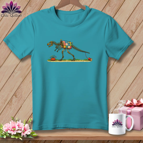 Teal t-shirt featuring a graphic of a skeletal dinosaur wearing a patchwork quilt and pulling thread.