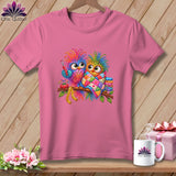 A pink t-shirt featuring two colorful cartoon owls on a branch with sewing accessories.