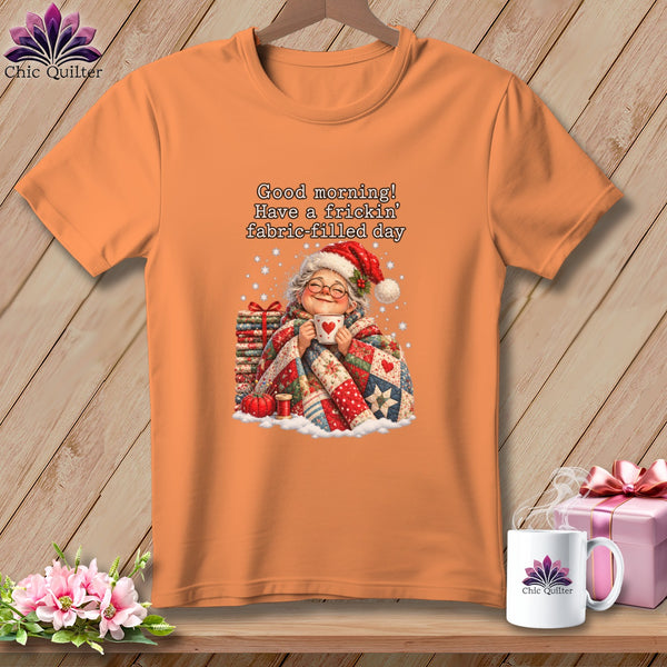 An orange t-shirt displays an illustrated graphic of an elderly woman holding a mug with text above her reading Good morning! Have a frickin fabric filled day.