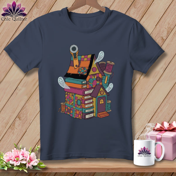 Dark t-shirt with a colorful quilt-themed house on books, featuring ghosts and sewing notions.