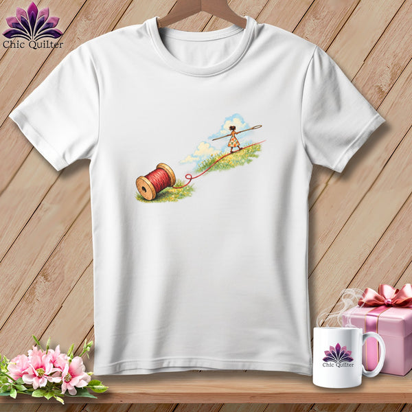 A white t-shirt features an illustration of a child tightrope walking on red thread extending from a spool.