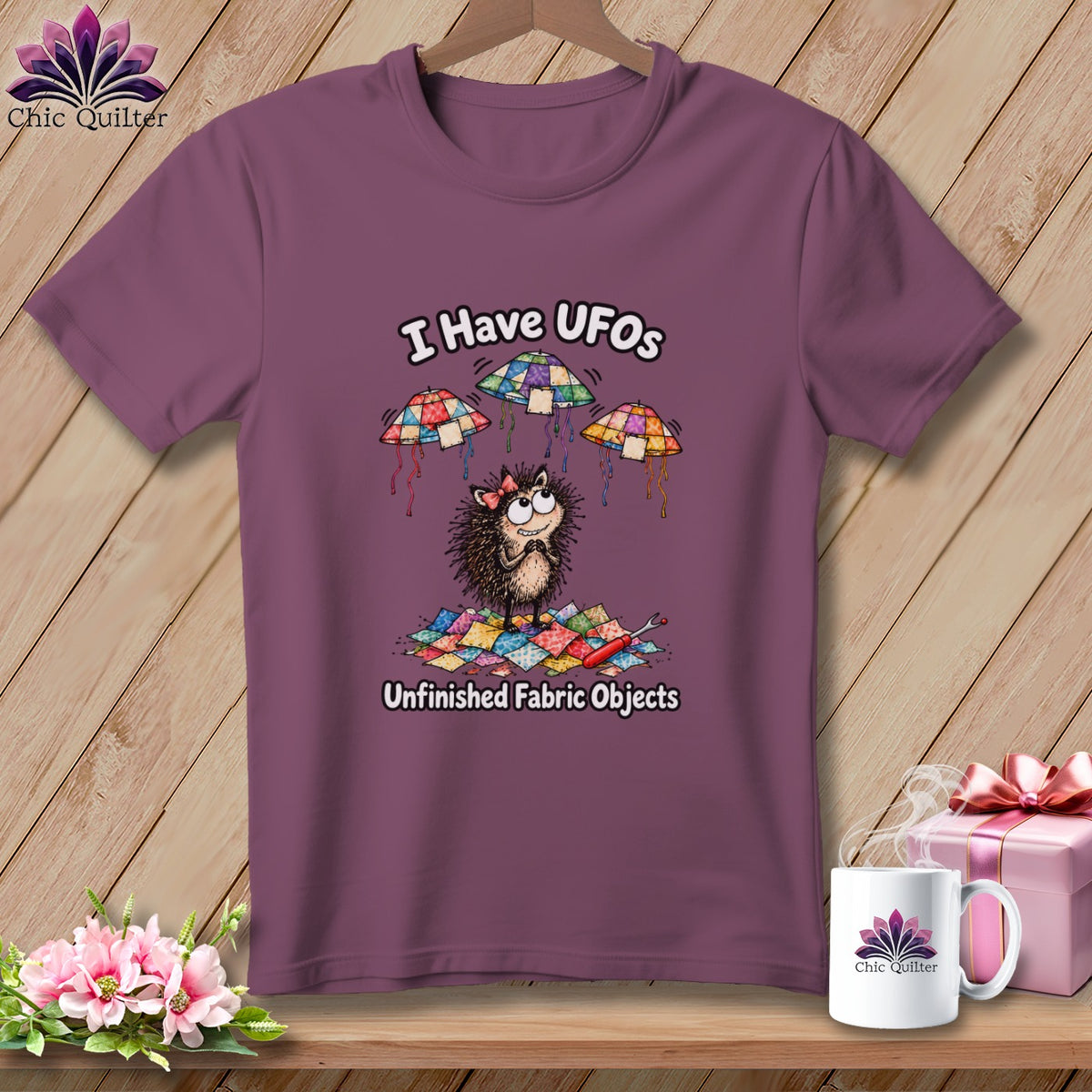Mauve t-shirt featuring a cartoon hedgehog, flying quilted UFOs, and the text I Have UFOs Unfinished Fabric Objects.