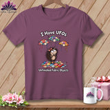 Mauve t-shirt featuring a cartoon hedgehog, flying quilted UFOs, and the text I Have UFOs Unfinished Fabric Objects.