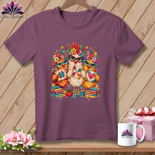 Plum-colored t-shirt featuring a graphic of three cute chickens wearing glasses and holding quilt blocks.