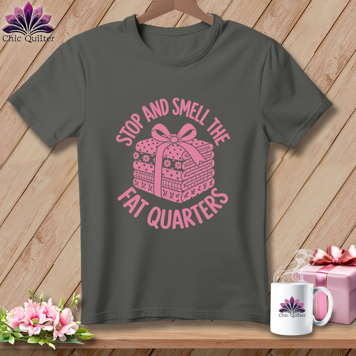 A dark gray t-shirt featuring a pink graphic of folded fabric with a bow and text reading stop and smell the fat quarters.