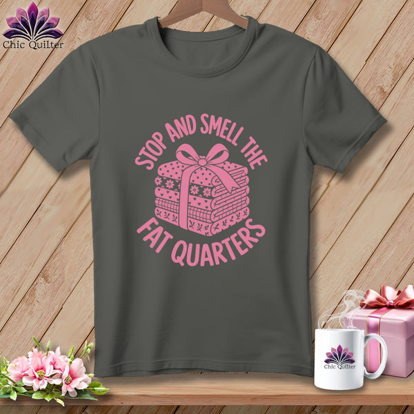 A dark gray t-shirt featuring a pink graphic of folded fabric with a bow and text reading stop and smell the fat quarters.
