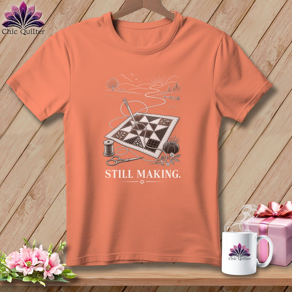 Peach t-shirt with a graphic of a quilt, sewing supplies, and the text "STILL MAKING."