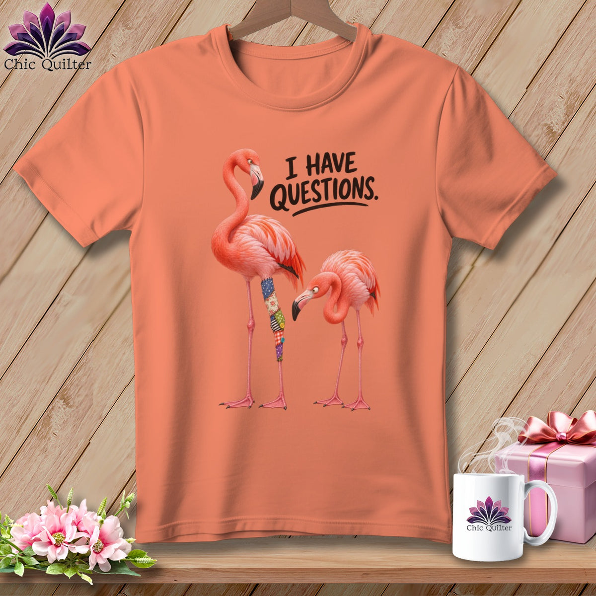 Peach t-shirt with two flamingos, one with a patchwork leg, and text "I HAVE QUESTIONS."