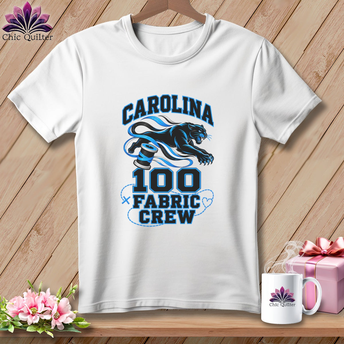 A white t-shirt hanging on a wooden background features a blue panther graphic with the text CAROLINA 100 FABRIC CREW.