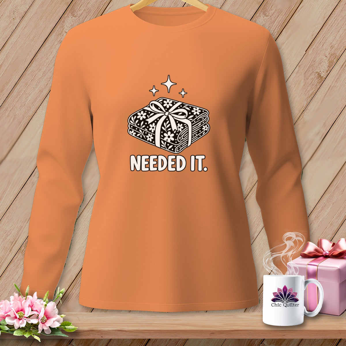 Orange long-sleeved shirt with a graphic of a fabric stack and "NEEDED IT." text.