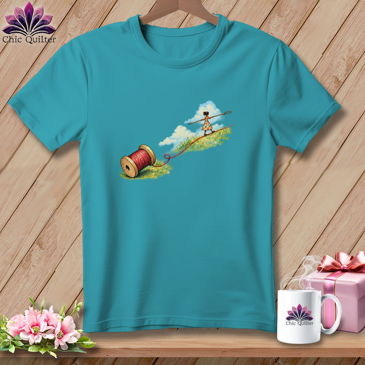 Teal crewneck t-shirt featuring an illustration of a spool of red thread and a girl walking on a tightrope.