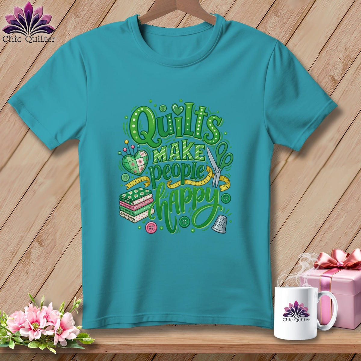 Teal short-sleeve t-shirt with a green typographic design that reads Quilts Make People Happy, decorated with sewing motifs.