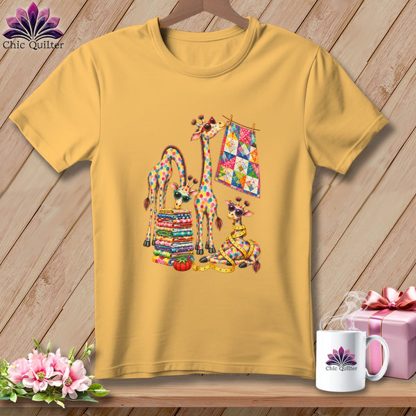 Gold crewneck t-shirt featuring a colorful graphic of giraffes with quilting patterns, stacks of fabric, and a hanging quilt.