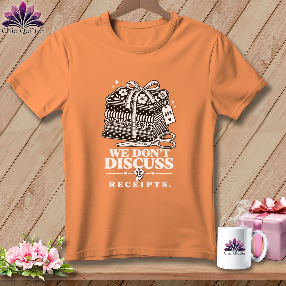 Orange t-shirt with stacked fabric, scissors, and "We Don't Discuss Receipts" text.
