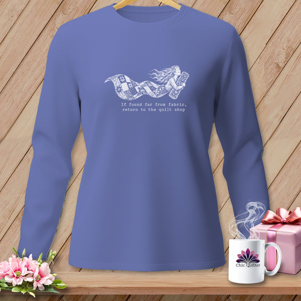 Periwinkle long-sleeved shirt with a graphic of a woman carrying fabric and the text "If found far from fabric, return to the quilt shop."