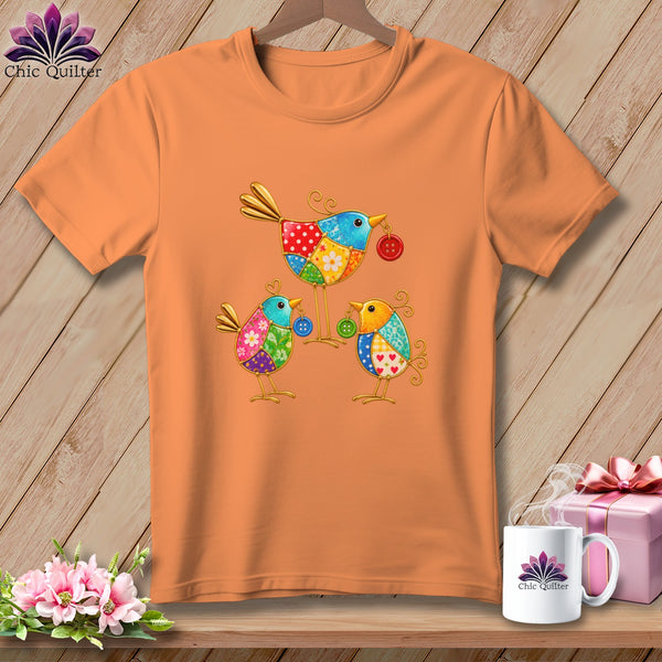 An orange crewneck t-shirt featuring a colorful graphic of three whimsical birds holding buttons.