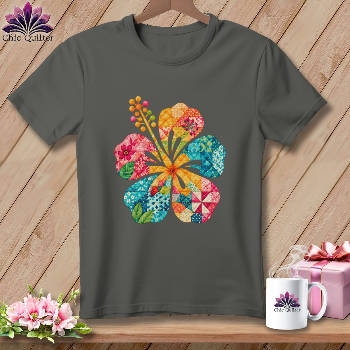 Charcoal gray t-shirt featuring a large, colorful hibiscus flower made of patchwork patterns, hanging on a wooden background.