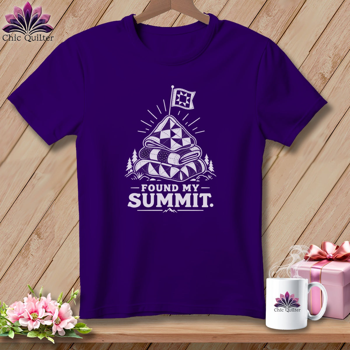 Purple t-shirt with a graphic of stacked quilts on a mountain peak with a flag.