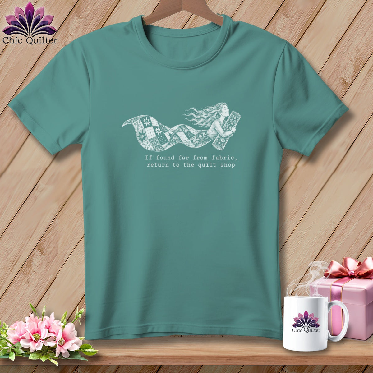 Teal t-shirt with a white graphic of a woman flying on a quilt banner and text.