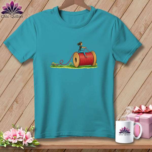 Teal short-sleeved t-shirt featuring a graphic of a person riding a giant red thread spool.
