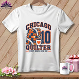 White t-shirt featuring a Chicago Quilter graphic with a stack of quilts, a coffee cup, and the number ten.