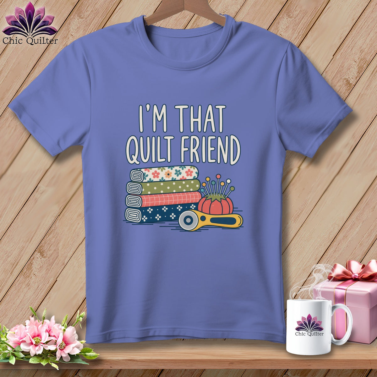 A purple t-shirt printed with the text I'm That Quilt Friend, stacked fabric, a pincushion, and a rotary cutter.