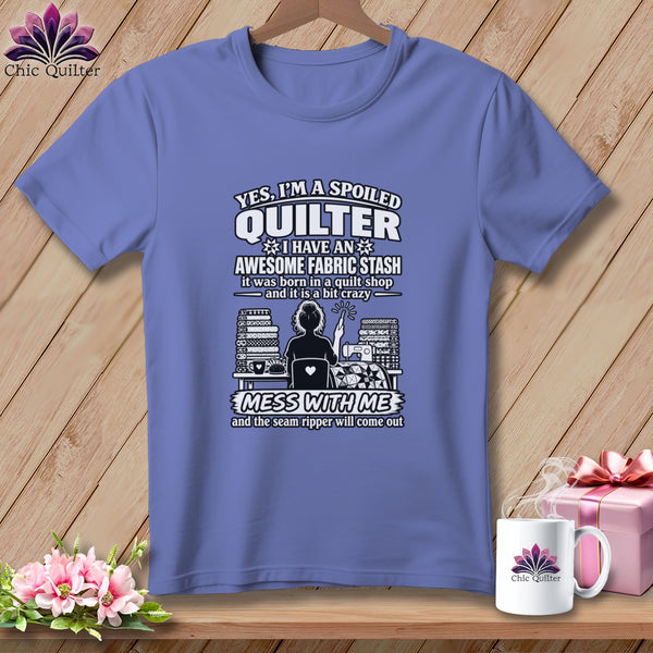 A periwinkle t-shirt on a wooden hanger with white text about a spoiled quilter and fabric stash.