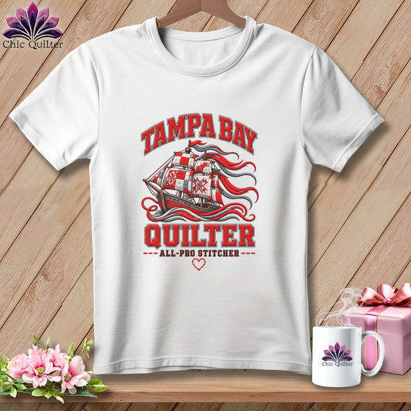 A white crewneck t-shirt with a graphic of a sailing ship, red patchwork sails, and Tampa Bay Quilter text.