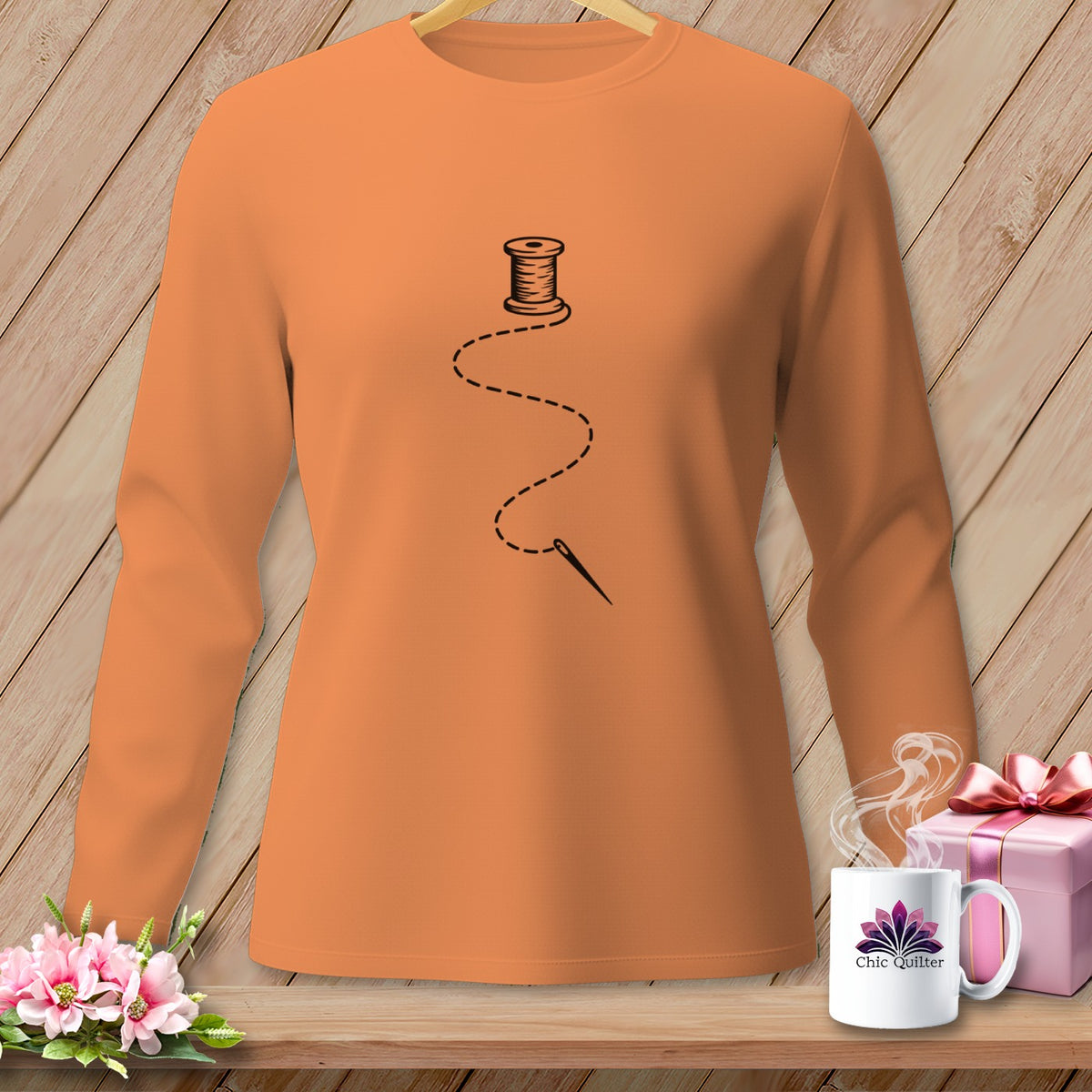 Orange long-sleeve shirt with black spool of thread, needle, and dashed line design.