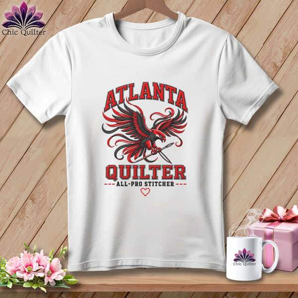 A white t-shirt featuring a red and black eagle graphic with sewing needles and Atlanta Quilter text.
