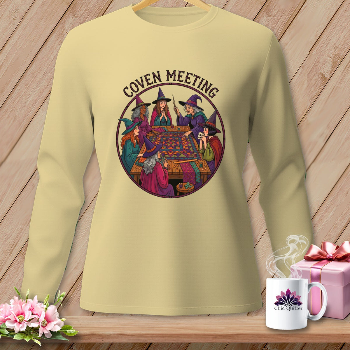 Crewneck sweatshirt with witches gathered around a quilt, text "Coven Meeting" above.