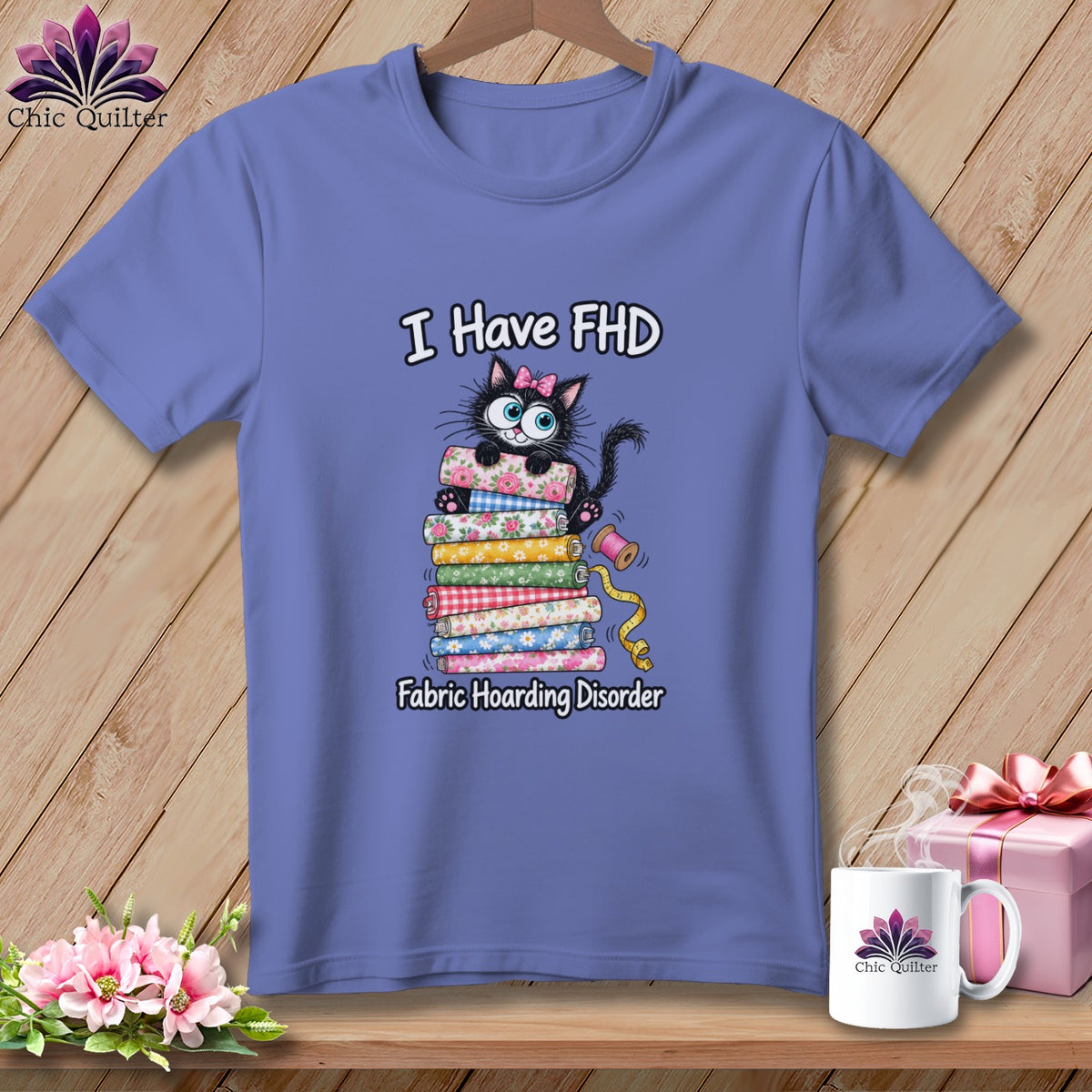 Periwinkle t-shirt on a hanger with a cartoon cat graphic and text reading I Have FHD Fabric Hoarding Disorder.