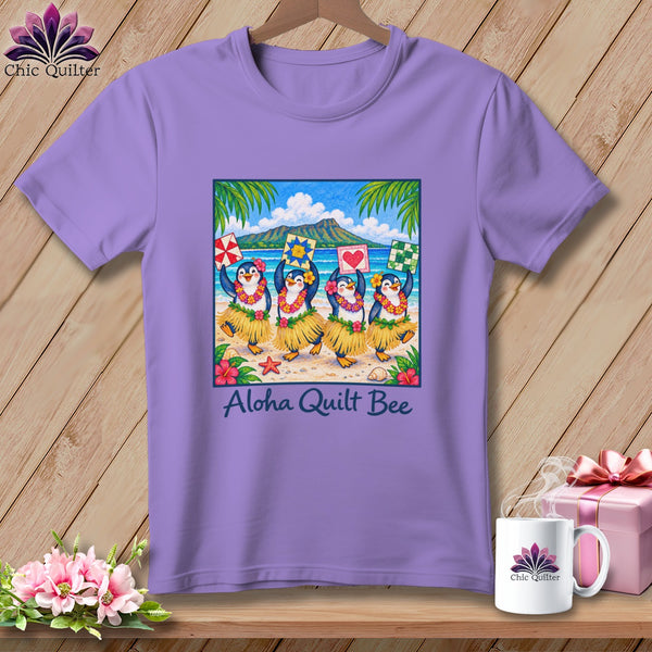A lavender crewneck t-shirt featuring a tropical beach graphic with dancing penguins holding quilt blocks, and the text Aloha Quilt Bee.