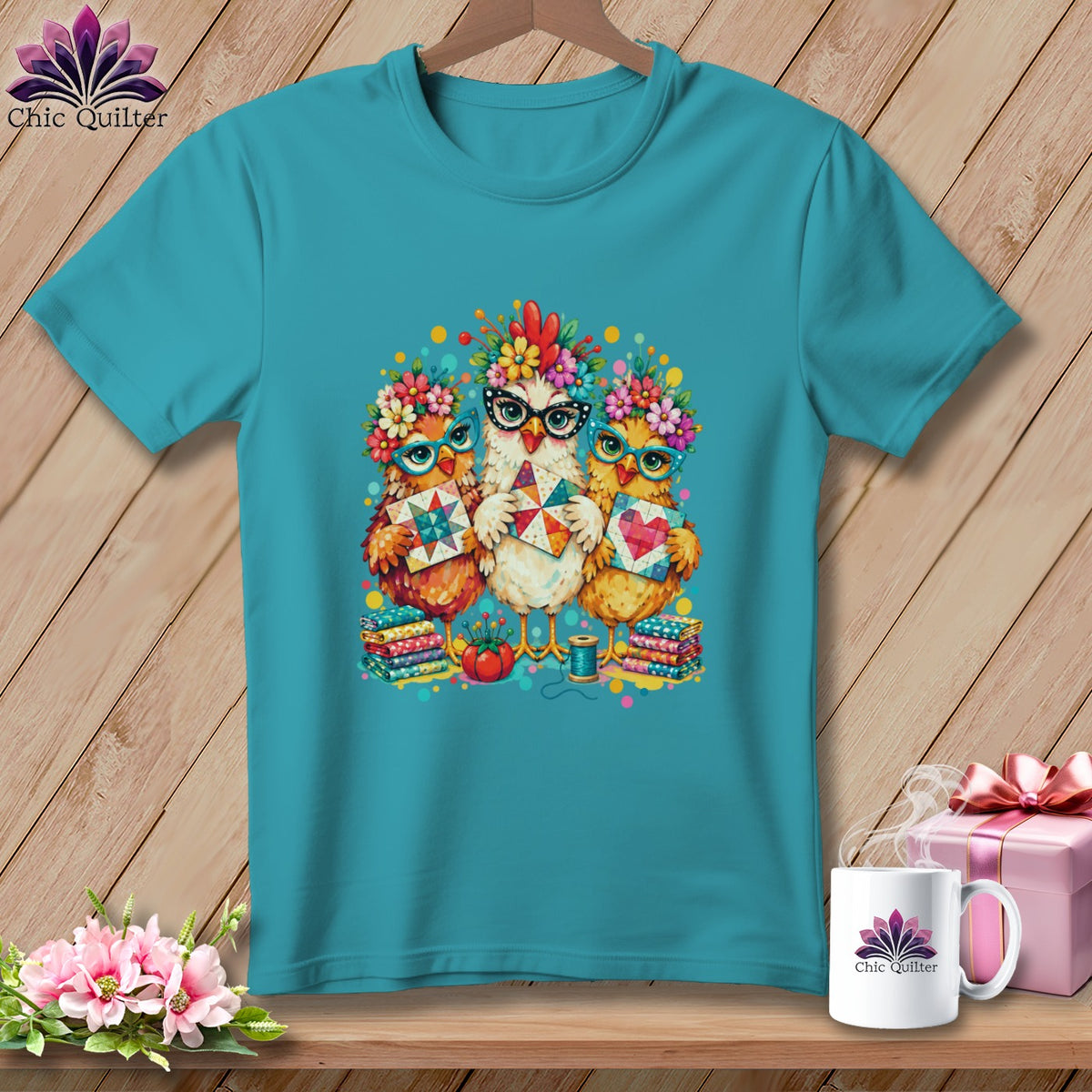 Teal t-shirt featuring a colorful graphic of three chickens wearing glasses and floral crowns while holding quilt blocks.